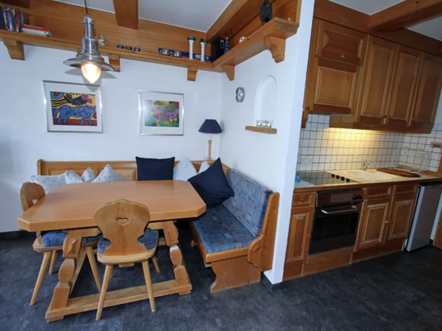 Holzküche mit Backofen und Kochfeld, daneben Essecke mit Eckbank, Tisch und Holzstühlen