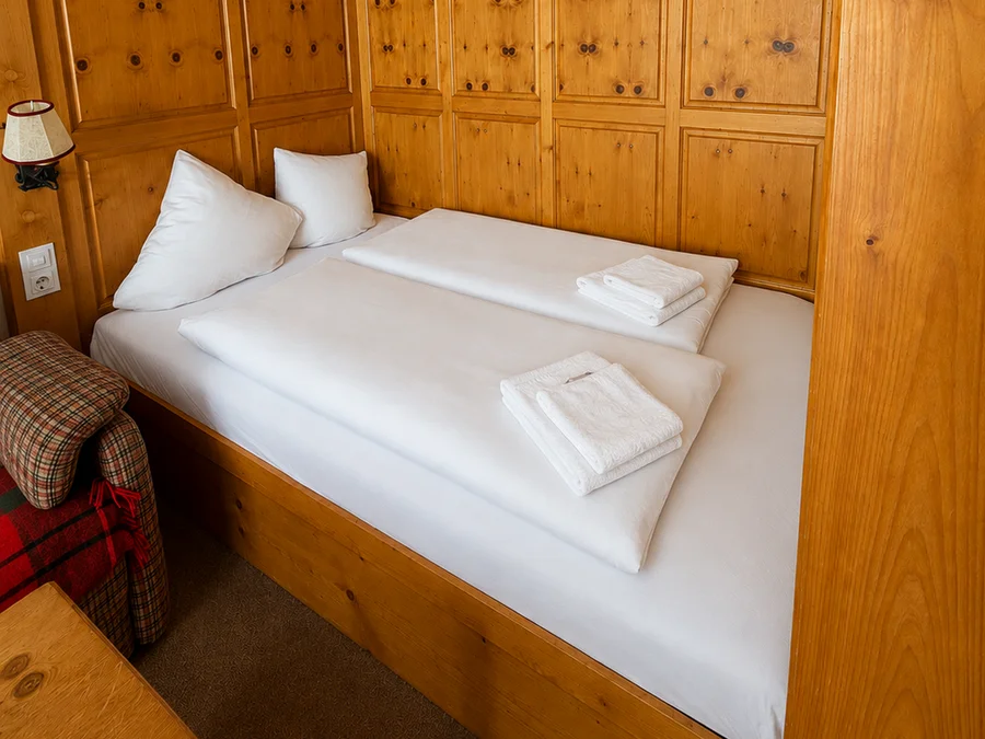 Doppelbett mit weißer Bettwäsche vor holzvertäfelter Wand mit Einbauschränken