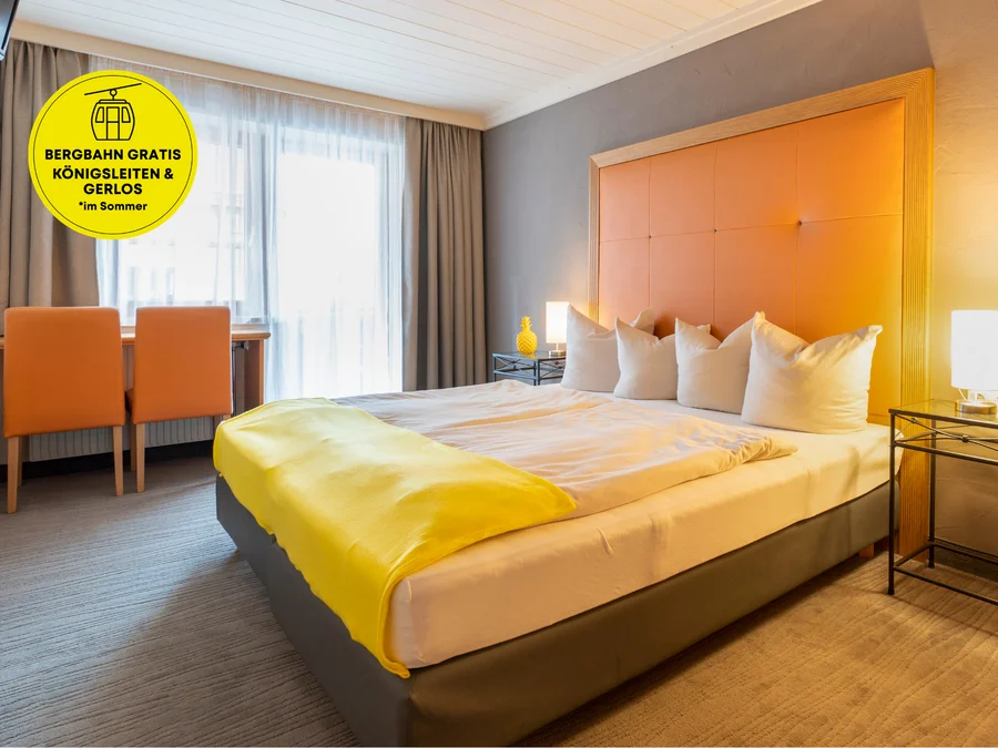 Premium Doppelzimmer mit gelber Tagesdecke, orangefarbenem Kopfteil, Schreibtisch und hellen Vorhängen