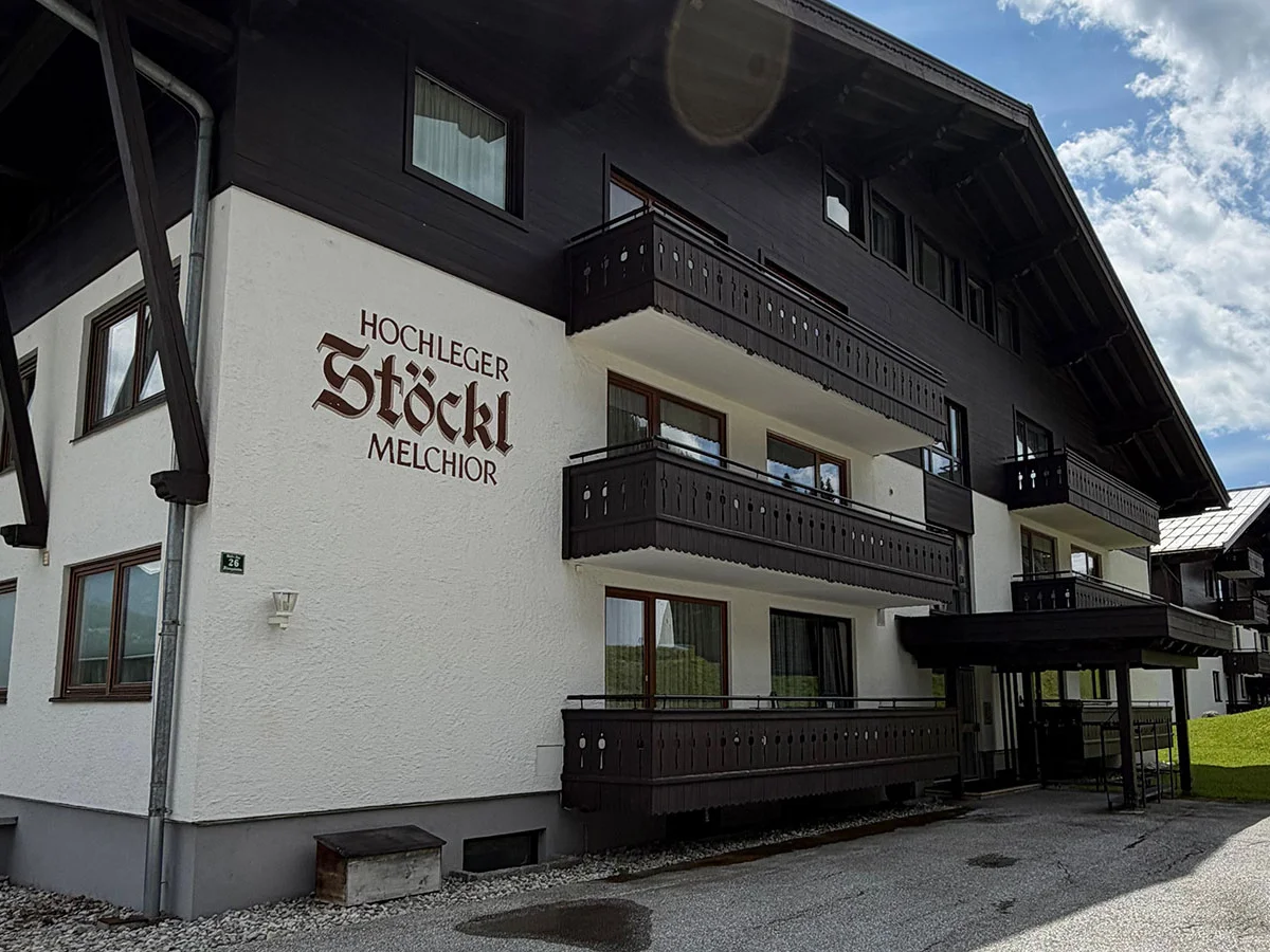Seitenansicht von Haus Stöckl mit Holzbalkonen und Eingang unter blauem Himmel