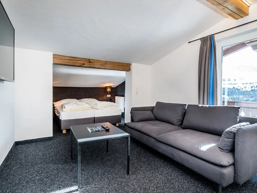 Heller Wohnbereich im Chalet H mit grauem Sofa, Couchtisch und Blick ins Schlafzimmer