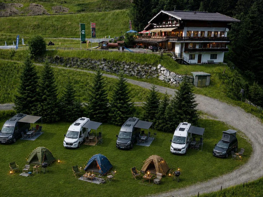 Luftaufnahme des Naturcampingplatzes mit Wohnmobilen, Zelten und Tannen, dahinter die Schönmoosalm