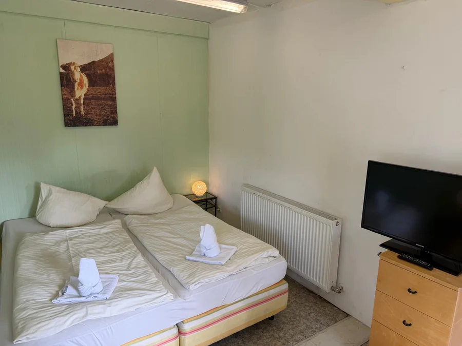 Doppelzimmer mit zwei zusammengestellten Betten, Flat-TV, Holzkommode und Kuhbild an der Wand