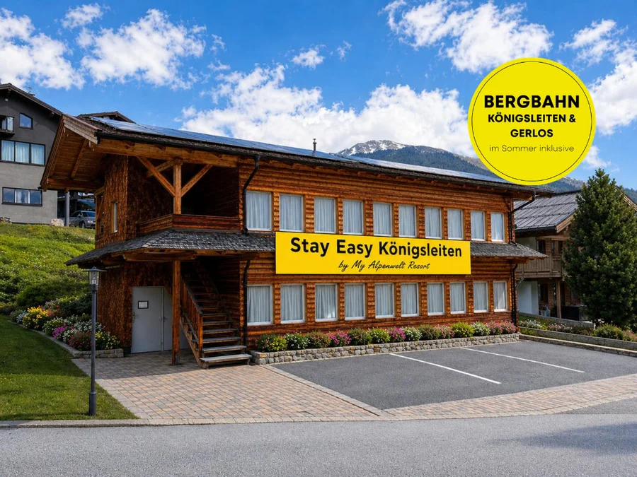Stay Easy Königsleiten by My Alpenwelt Resort: Holzhaus mit Außentreppe und Parkplätzen vor Bergen